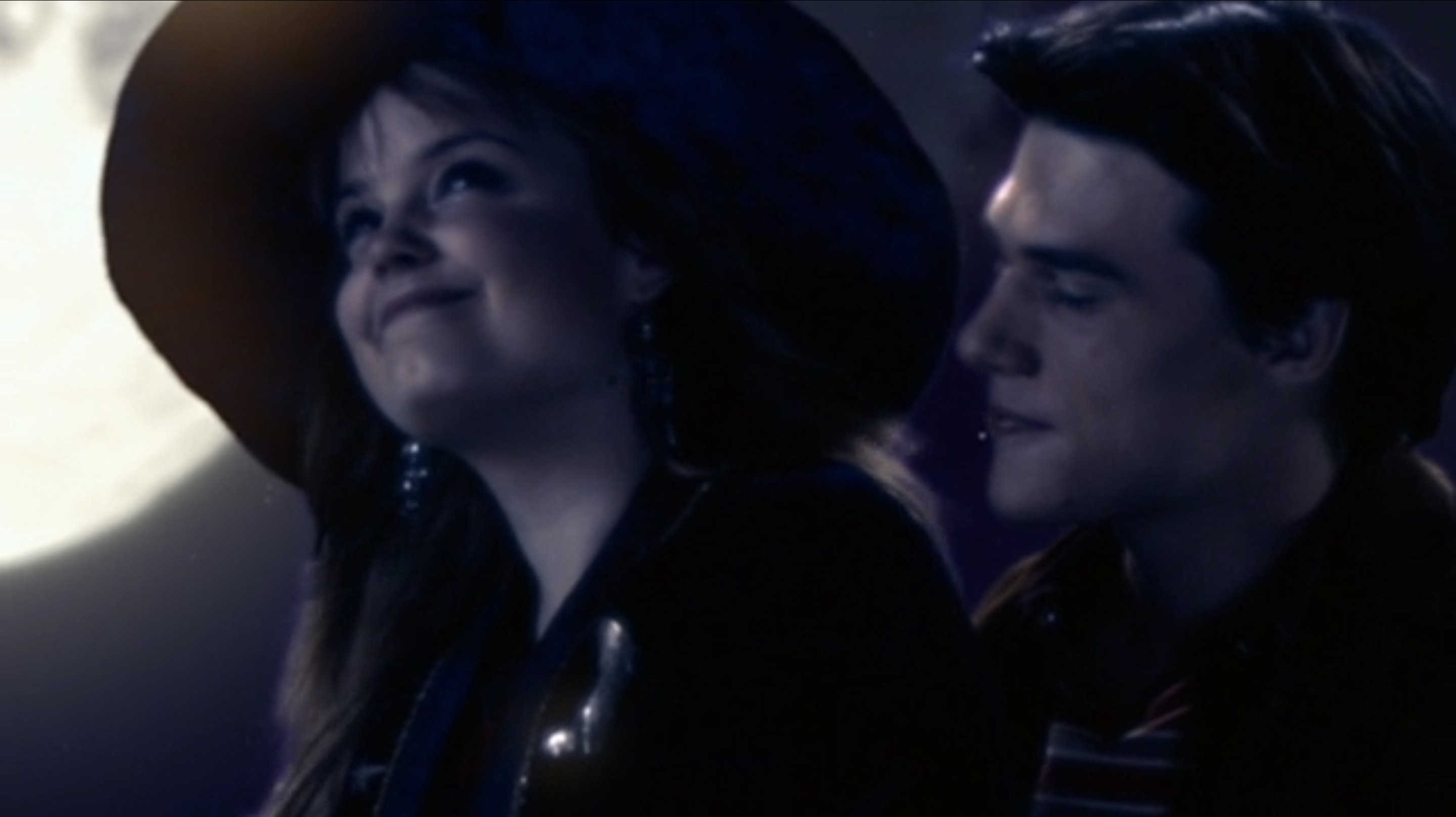 Kimberly J. Brown as Marnie Piper wears a wide brim hat and smiles at the night sky with Finn Wittrock as Cody behind her in &quot;Halloweentown High&quot;