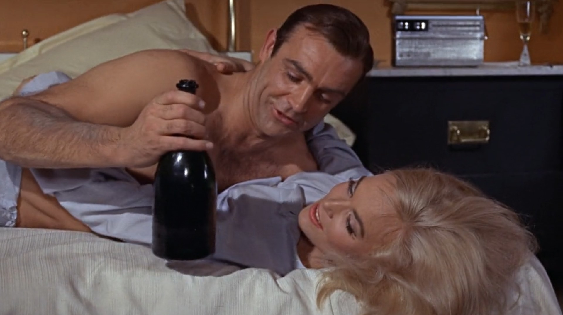 James Bond holding a bottle of champagne and lies on top of a woman