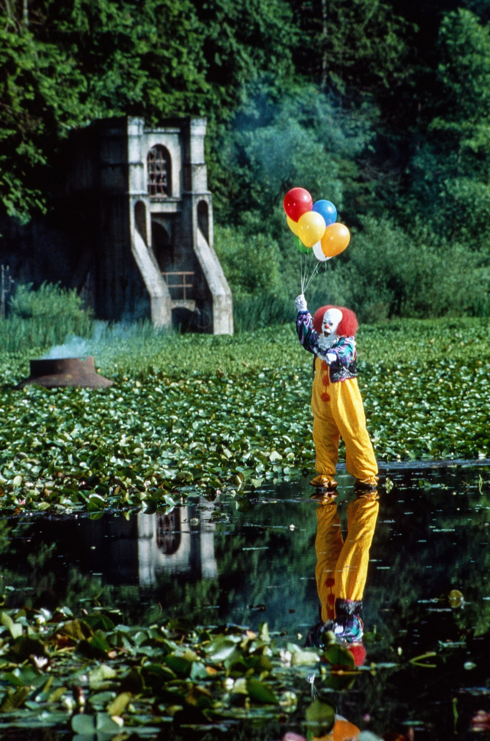 Pennywise holding balloons while standing on the surface of a lake