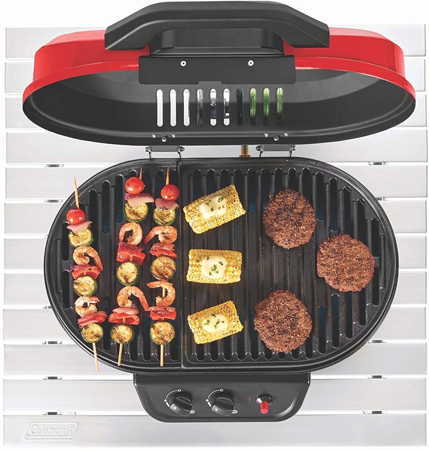 Red portable grill with kebabs, corn, and burgers cooking on it