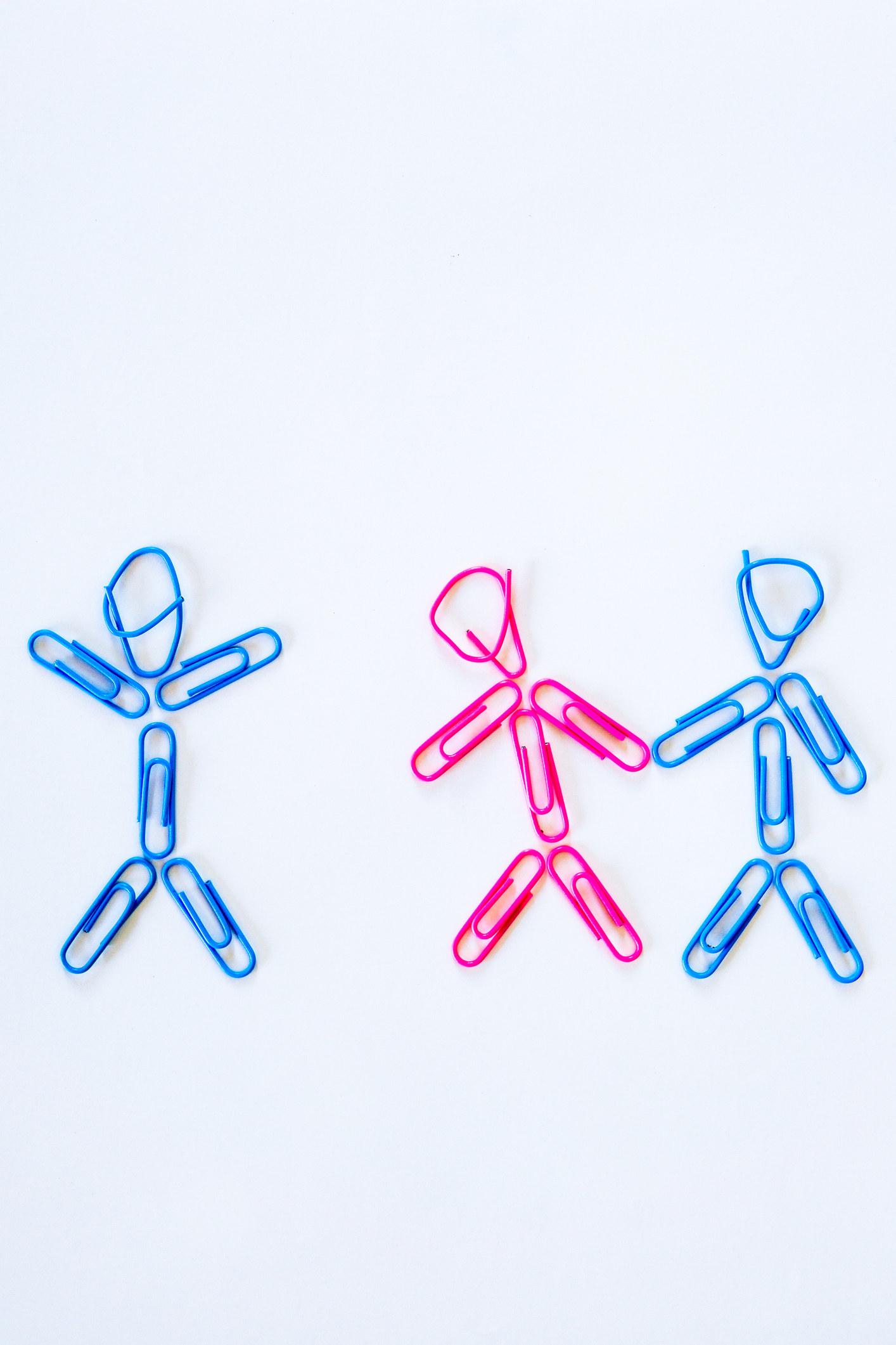 a stick figure couple made of paper clips together, then one of the figures reaching towards another third stick figure