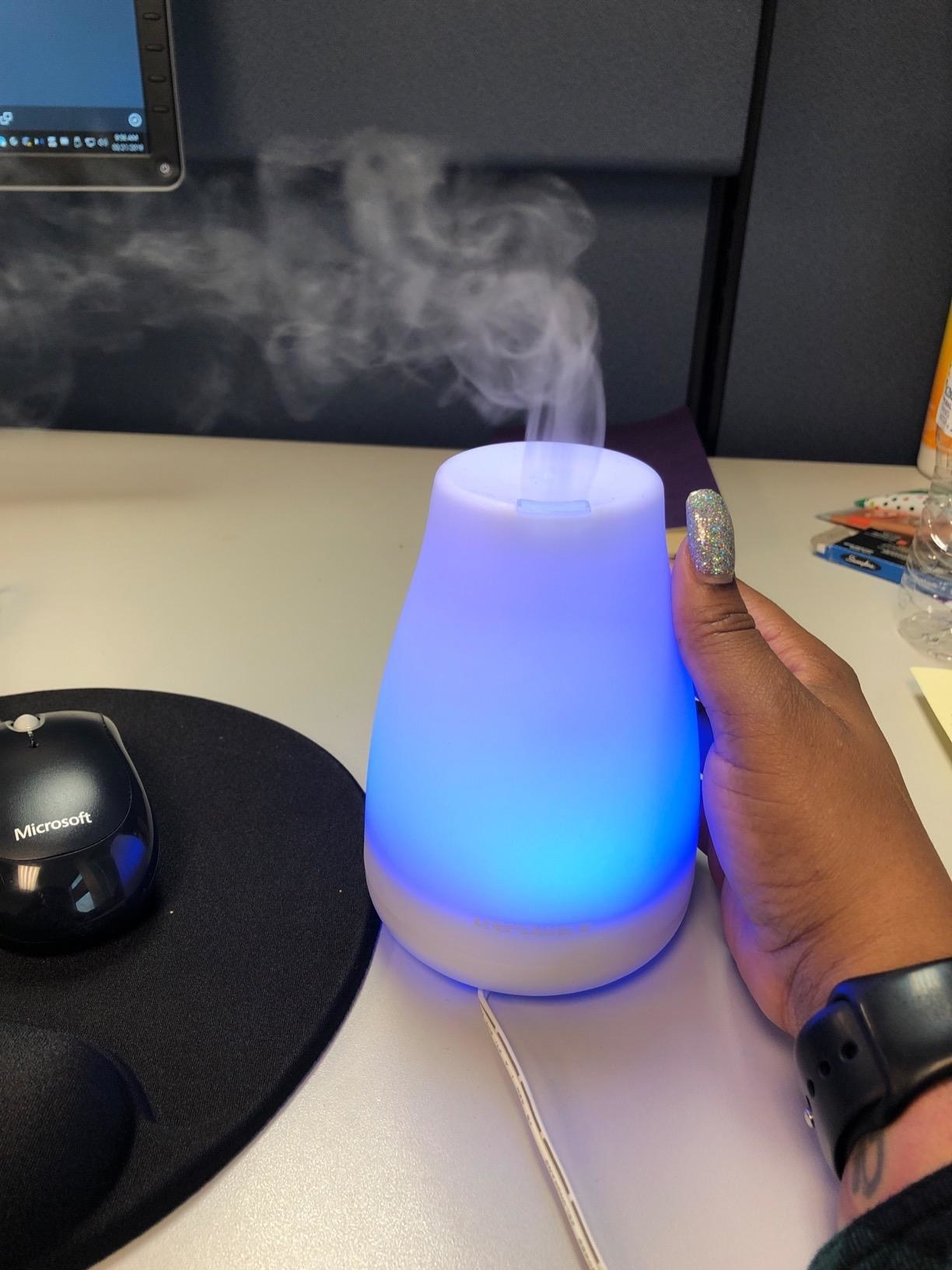 reviewer holds mini diffuser with a blue light next to work desk