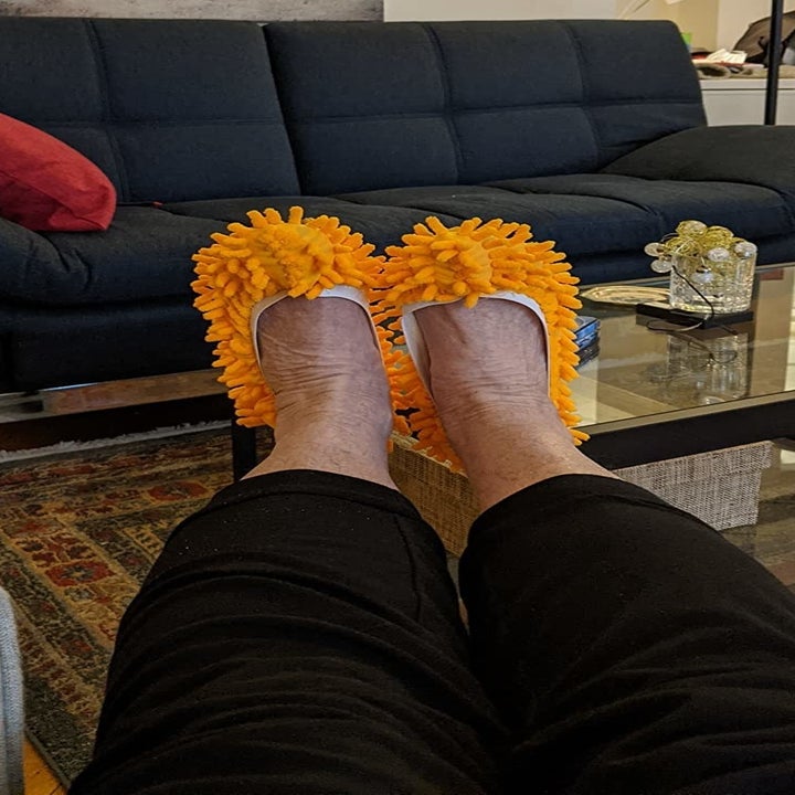 reviewer wears light orange mop slippers while sitting on couch