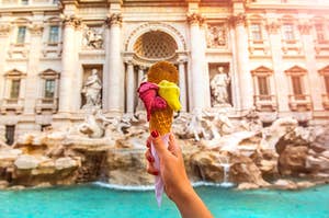 A woman is holding up an ice cream cone in front of a fountain in Italy