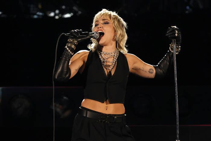 Miley performs on stage while wearing a black vest