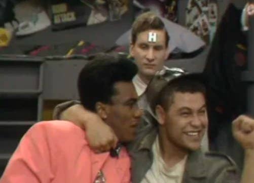 Lister wraps his arm around the Cat with a joyful expression while Rimmer looks on in disgust