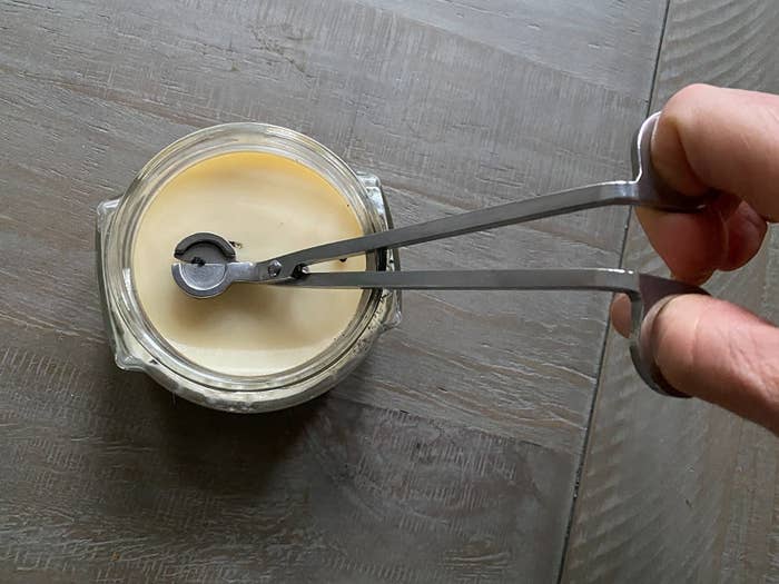 reviewer using the wick cutter in a candle to trim the wick