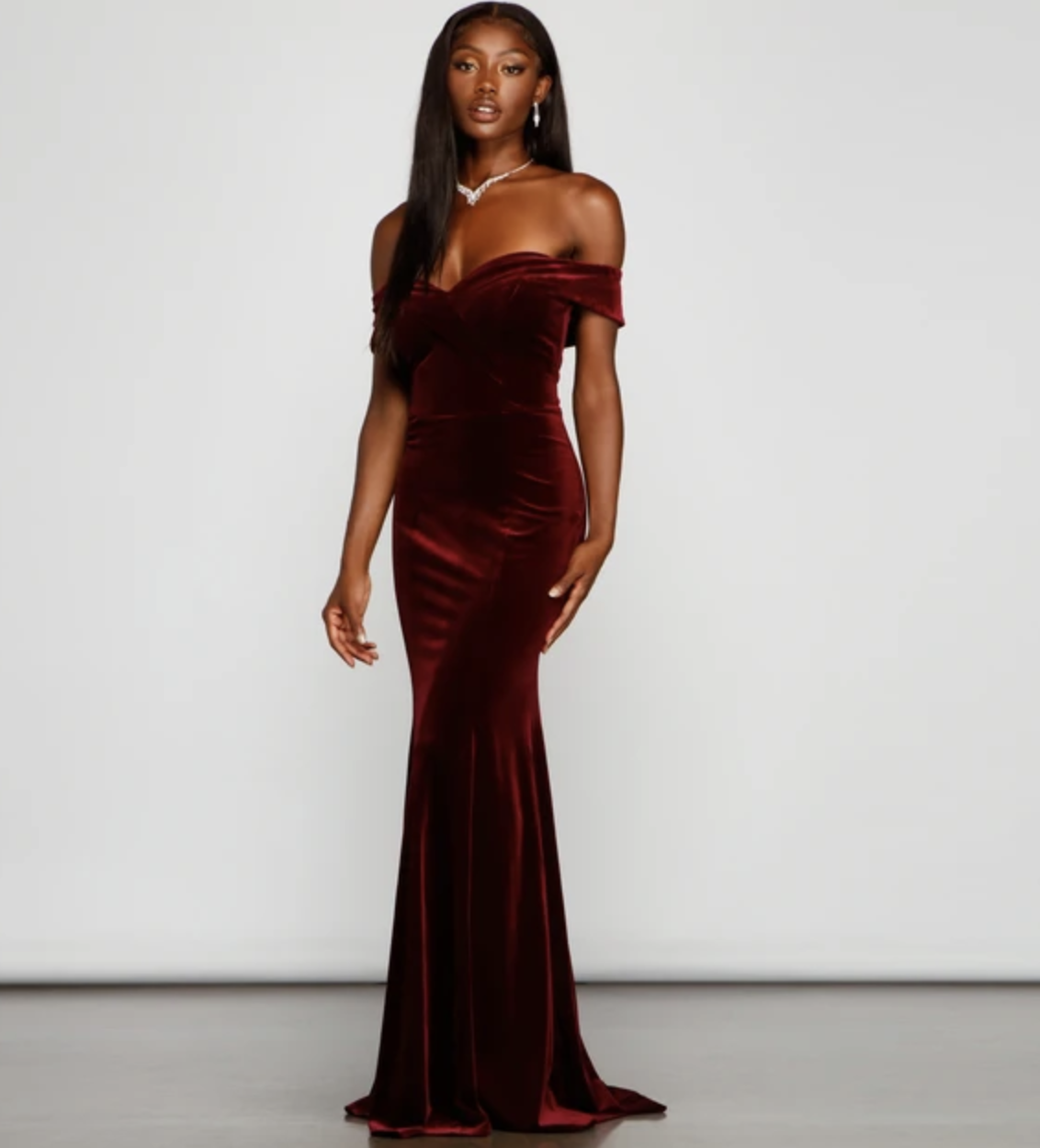 a model in an off the shoulder burgundy velvet gown