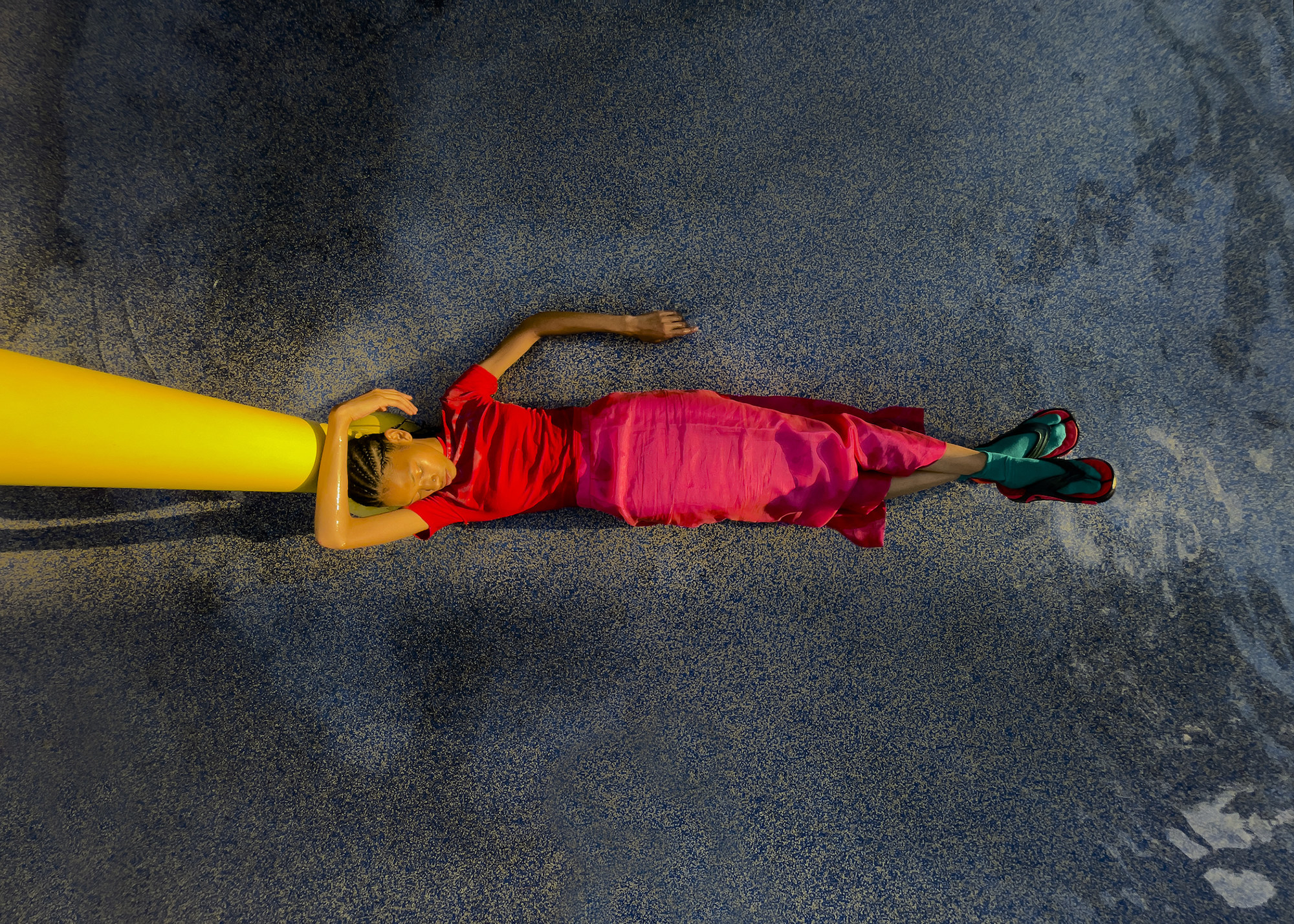 A figure in a red shirt and shirt lying at the foot of a pillar, seen from above