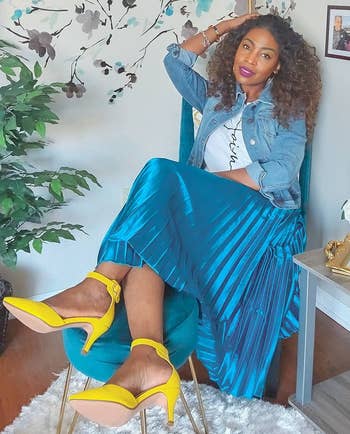a reviewer sitting in a chair wearing the midi skirt in blue with a T-shirt and yellow heels