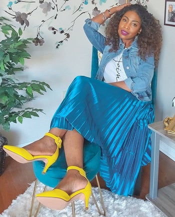 a reviewer sitting in a chair wearing the midi skirt in blue with a T-shirt and yellow heels