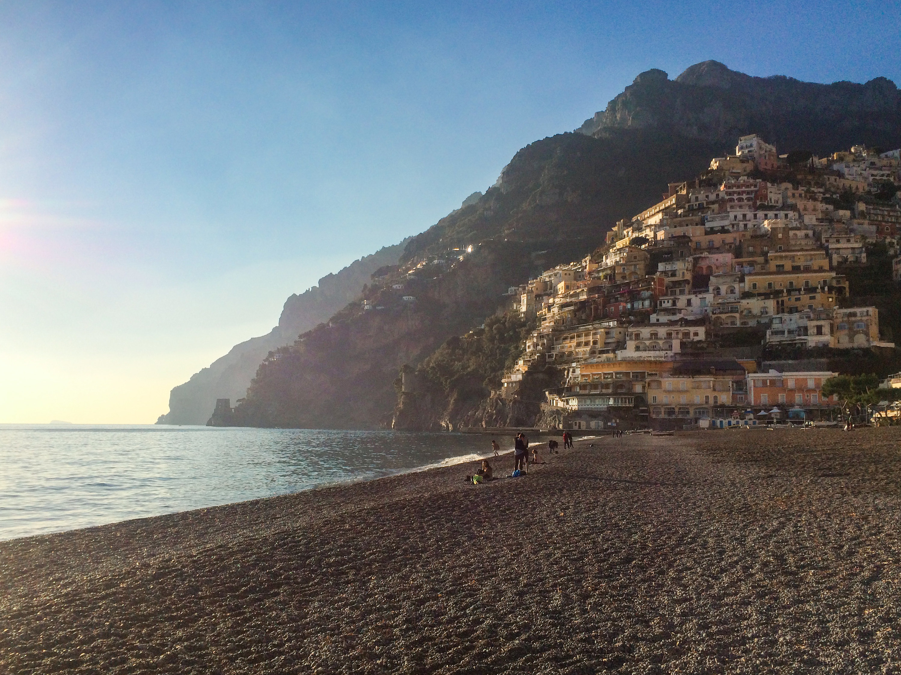 Beach in Positano with beautiful mountain leading out to the ocean and stacked houses perched in a pyramid-like-shape.