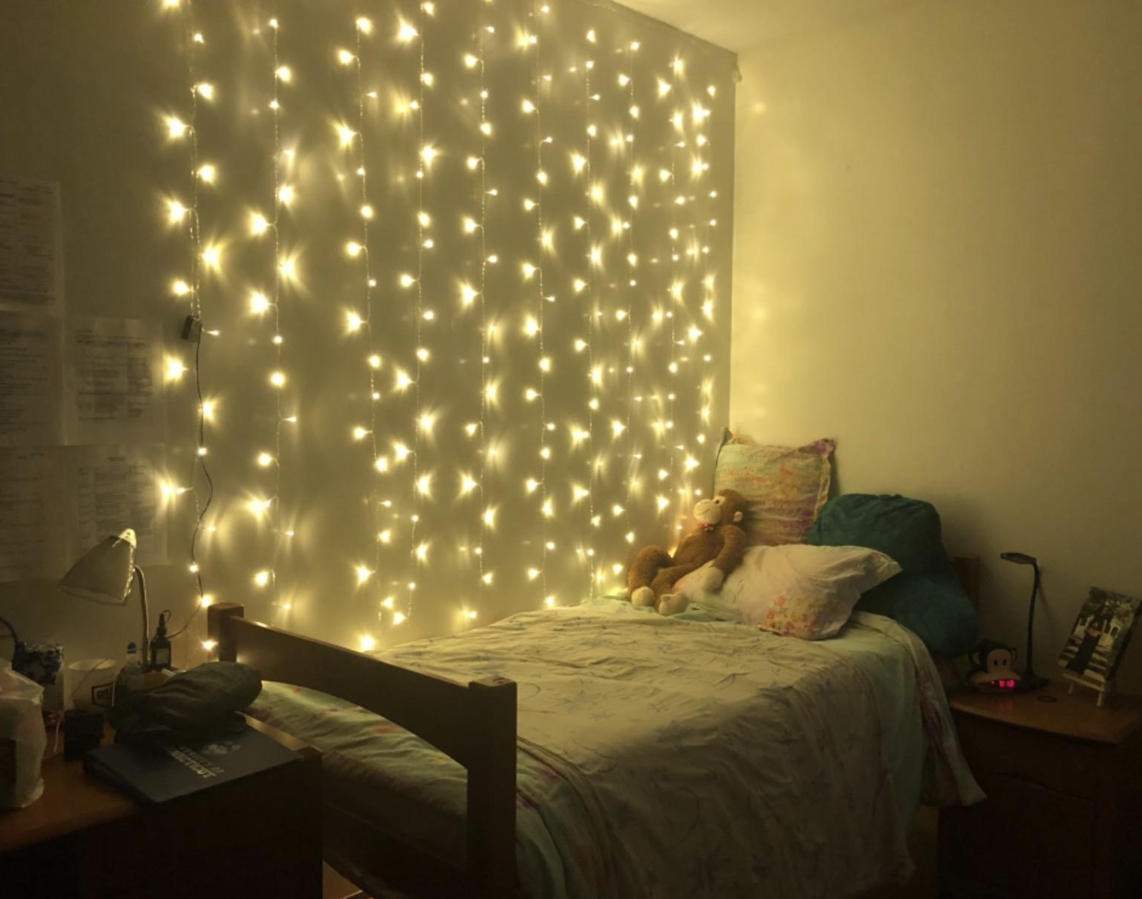 reviewer's yellow-toned string light curtain behind their bed