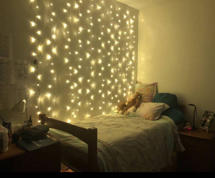 reviewer&#x27;s yellow-toned string light curtain behind their bed