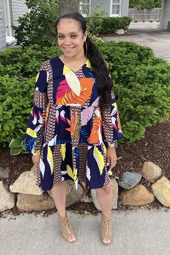 a reviewer wearing the dress in a multicolored print with lace-up heels