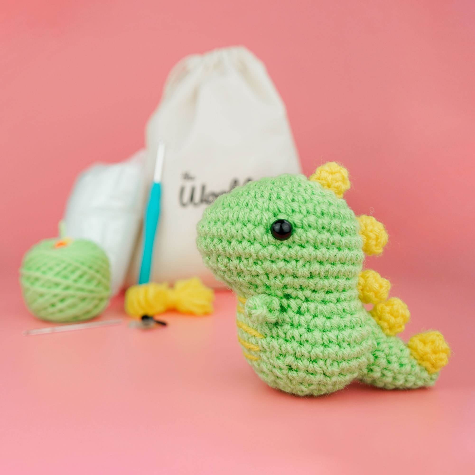 a crochet green dinosaur plushie with the full kit in the background