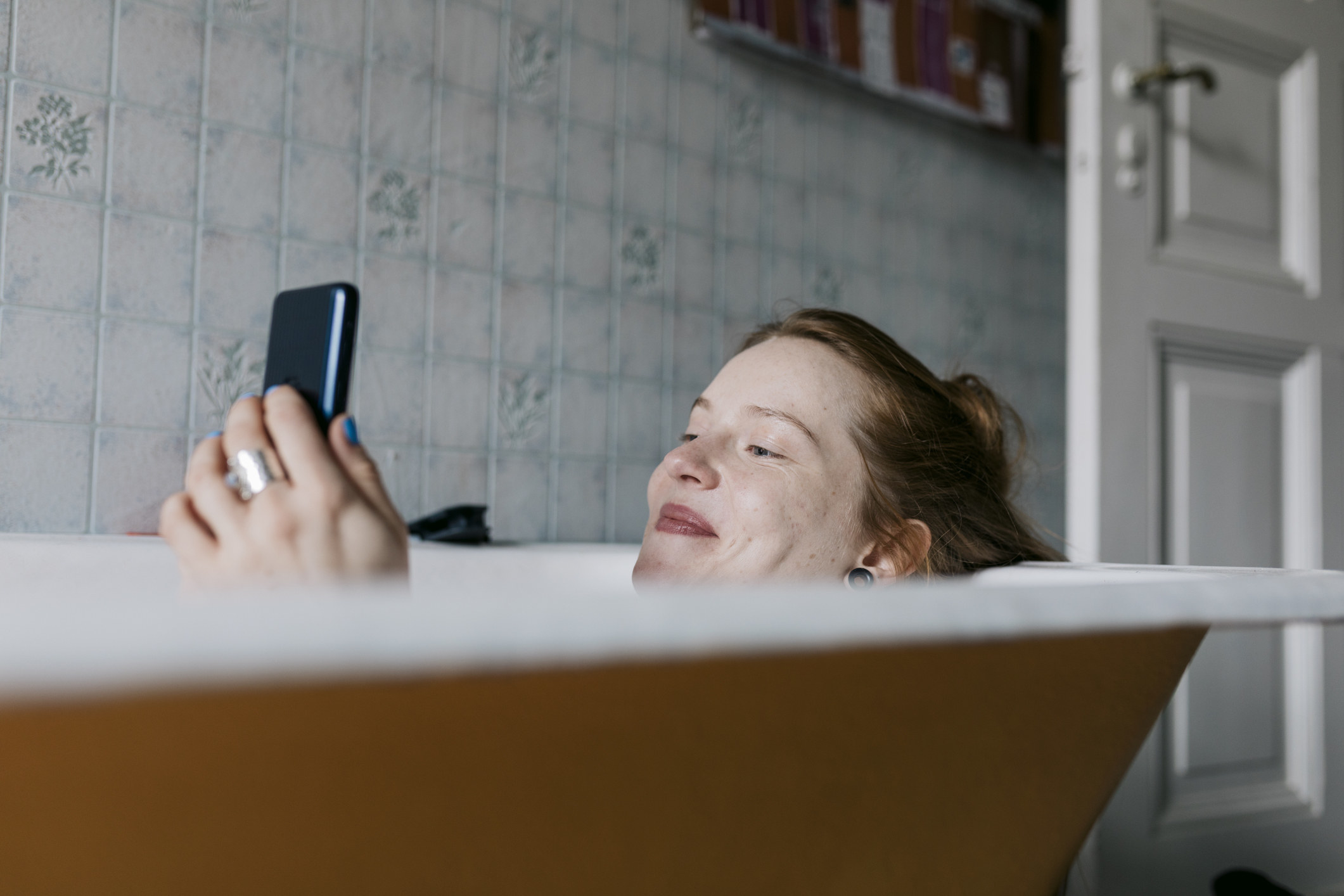 Someone relaxes in a tub while watching something on their phone