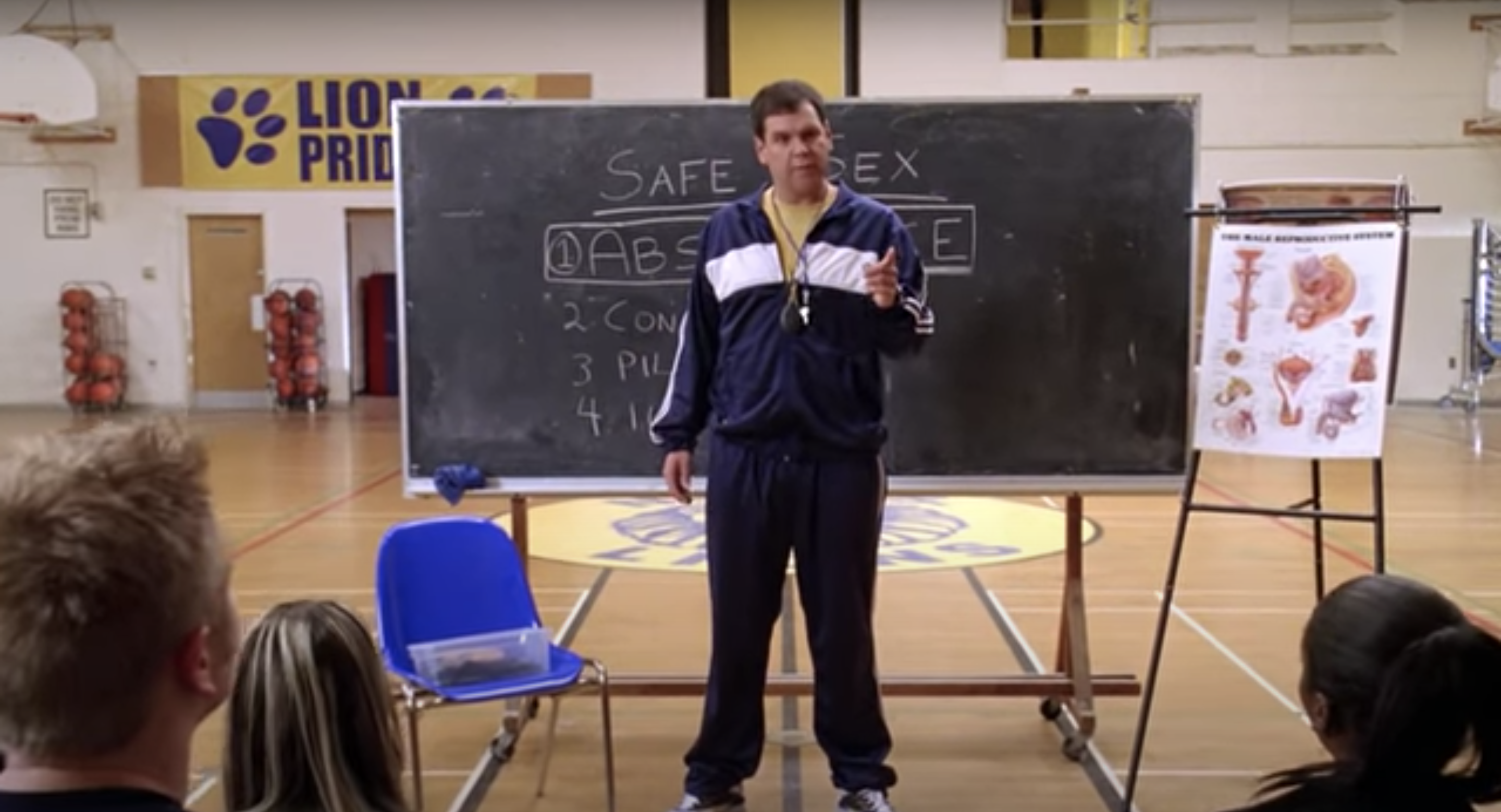 A teacher points in front of a chalkboard reading Safe Sex