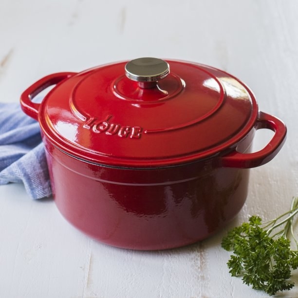 the red dutch oven next to herbs and a kitchen towel