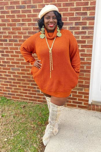 a reviewer wearing the sweater dress in orange with thigh-high boots