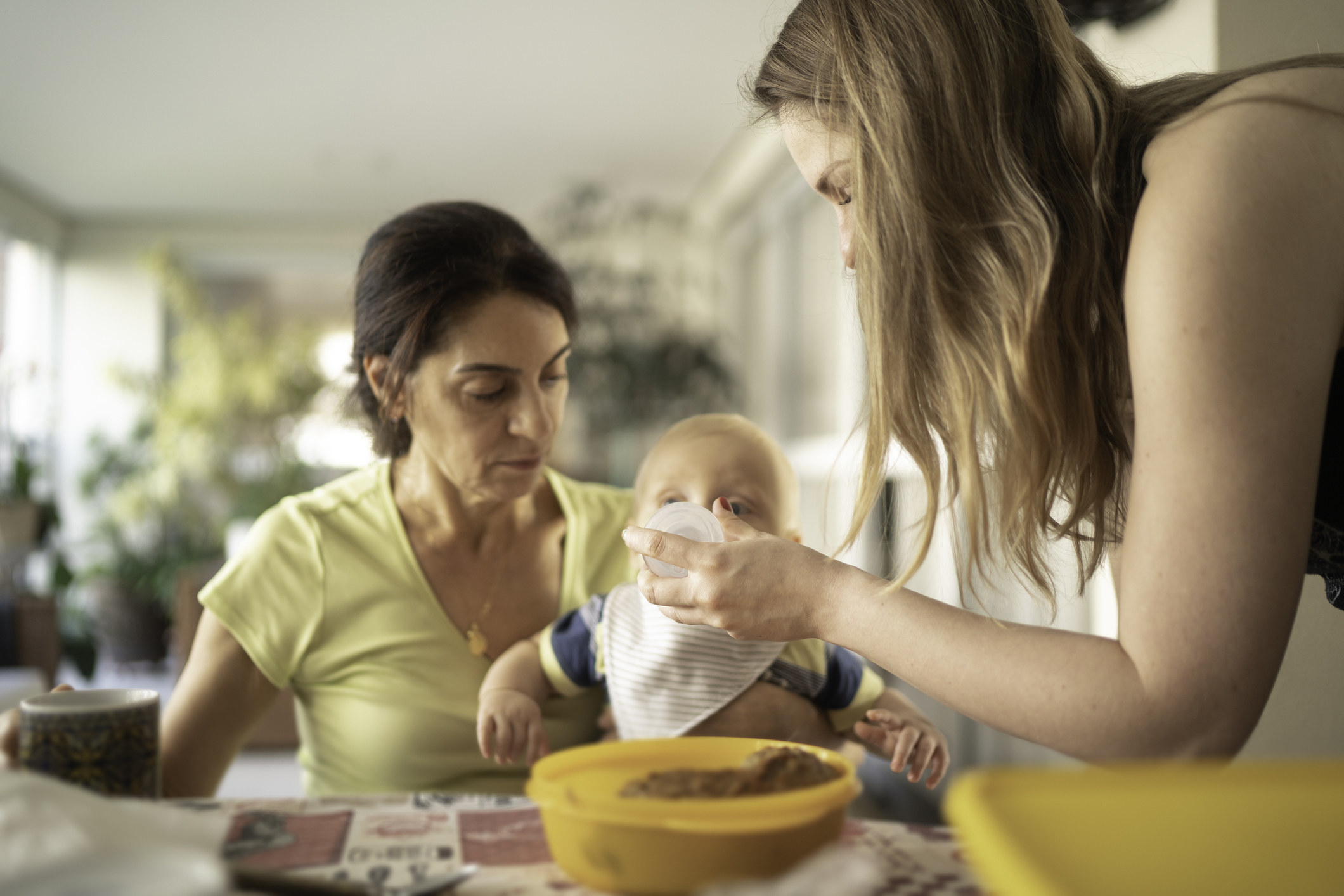 A grandma watches and a mother feeds her baby.