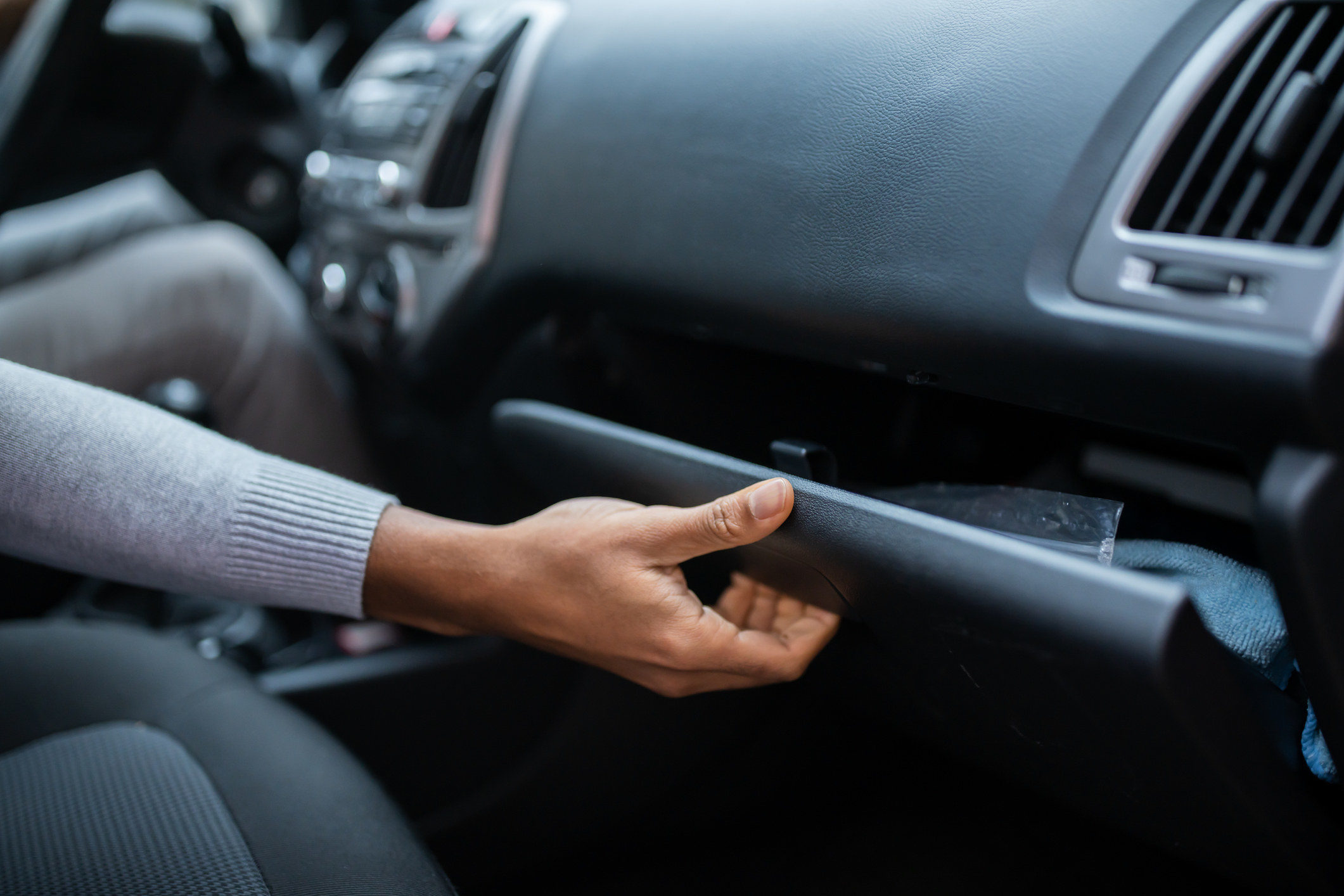 A hand opens the glove compartment of a car.