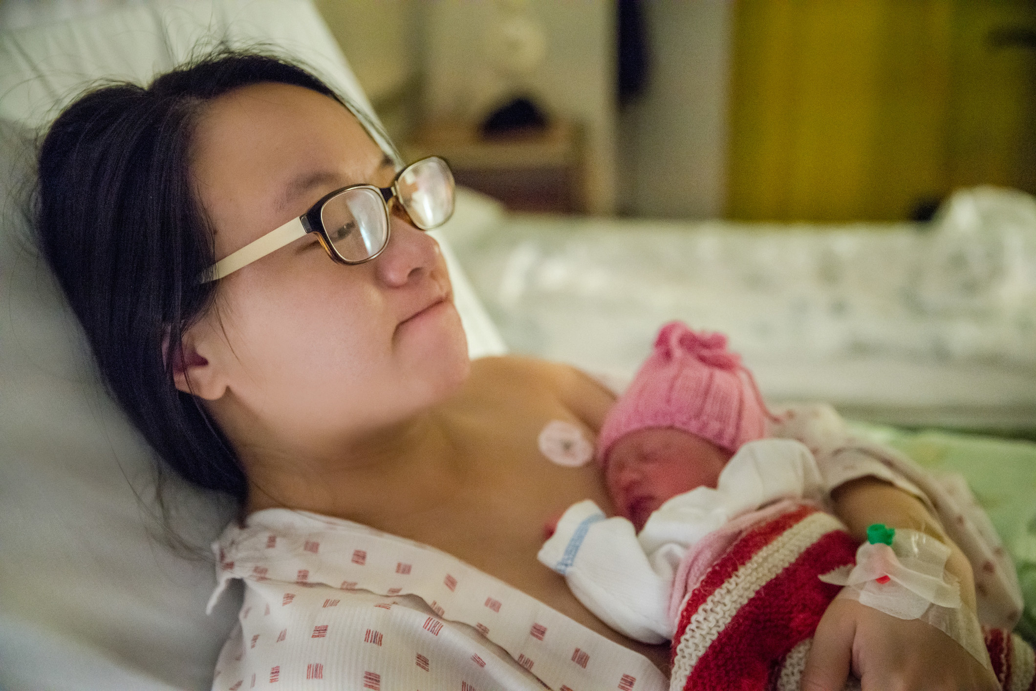 A mother lies in a hospital bed with her newborn lying on her chest.