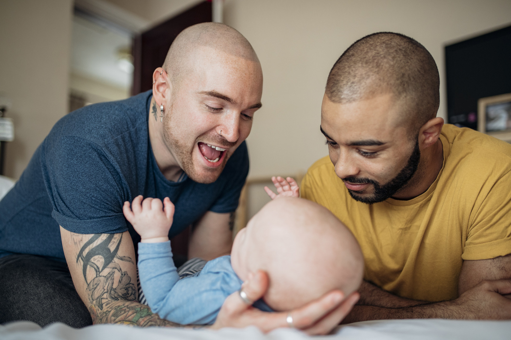 Two fathers happily play with their baby.