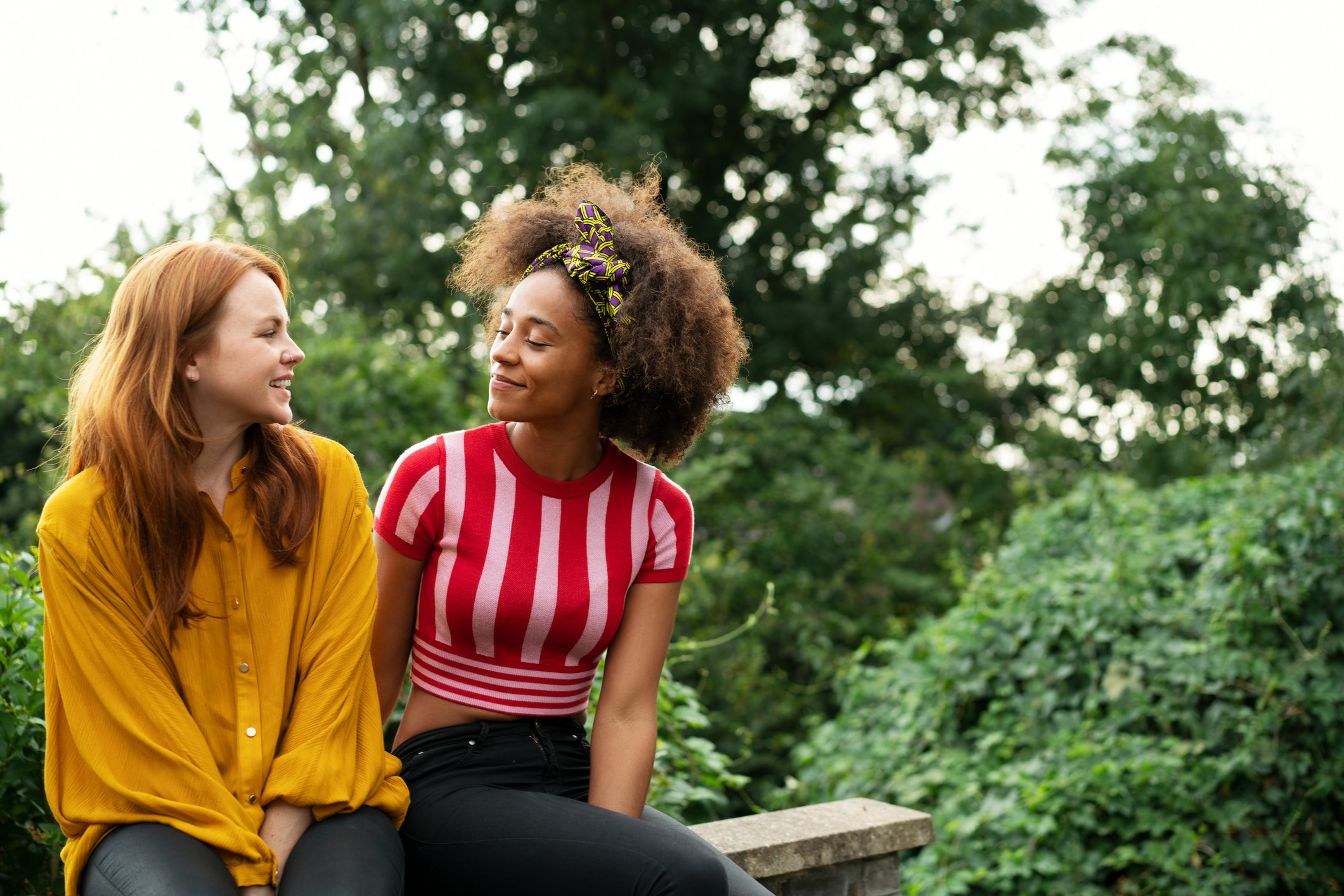 Two women are talking while sitting closely together on a bench.