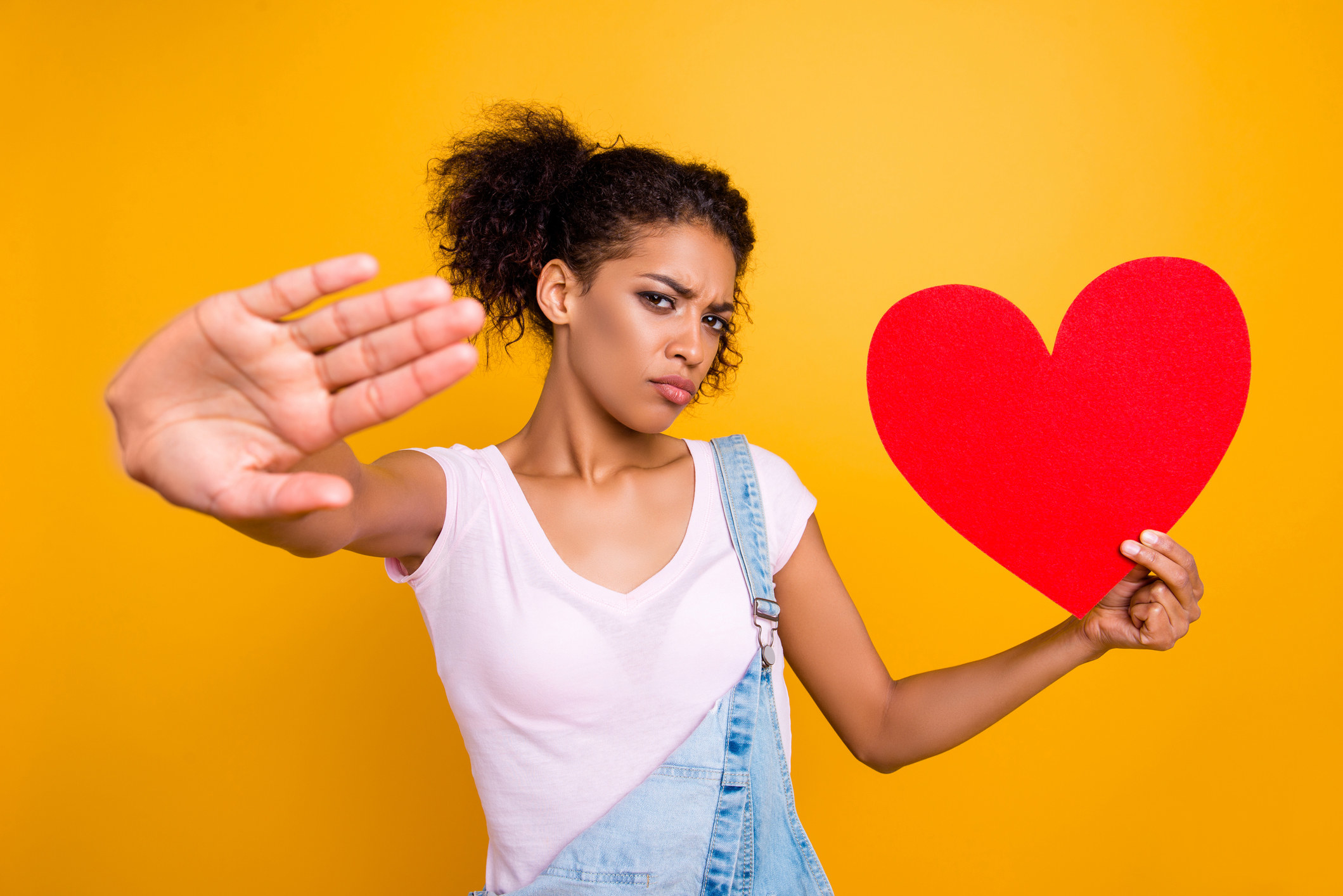 A woman holds up her hand as if to block off the world, while holding a heart in the other hand.