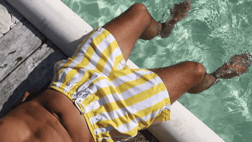 A man laying by the pool in yellow and white striped bathing suit shorts