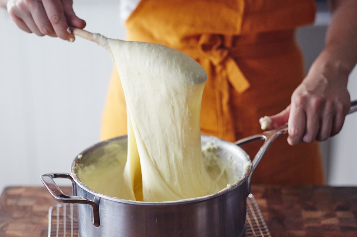 Cheesy potatoes being mixed and stretched with a wooden spoon
