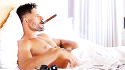 Joe Manganiello laying in bed shirtless with a cigar in his mouth