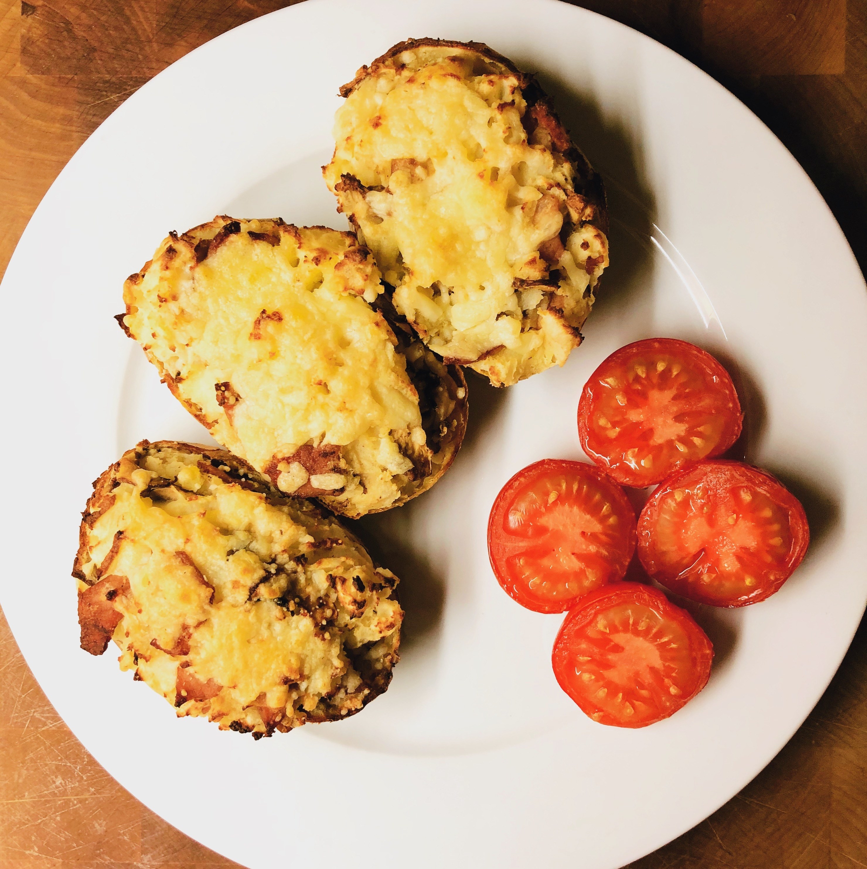 twice baked potatoes on a serving plate with sliced tomatoes