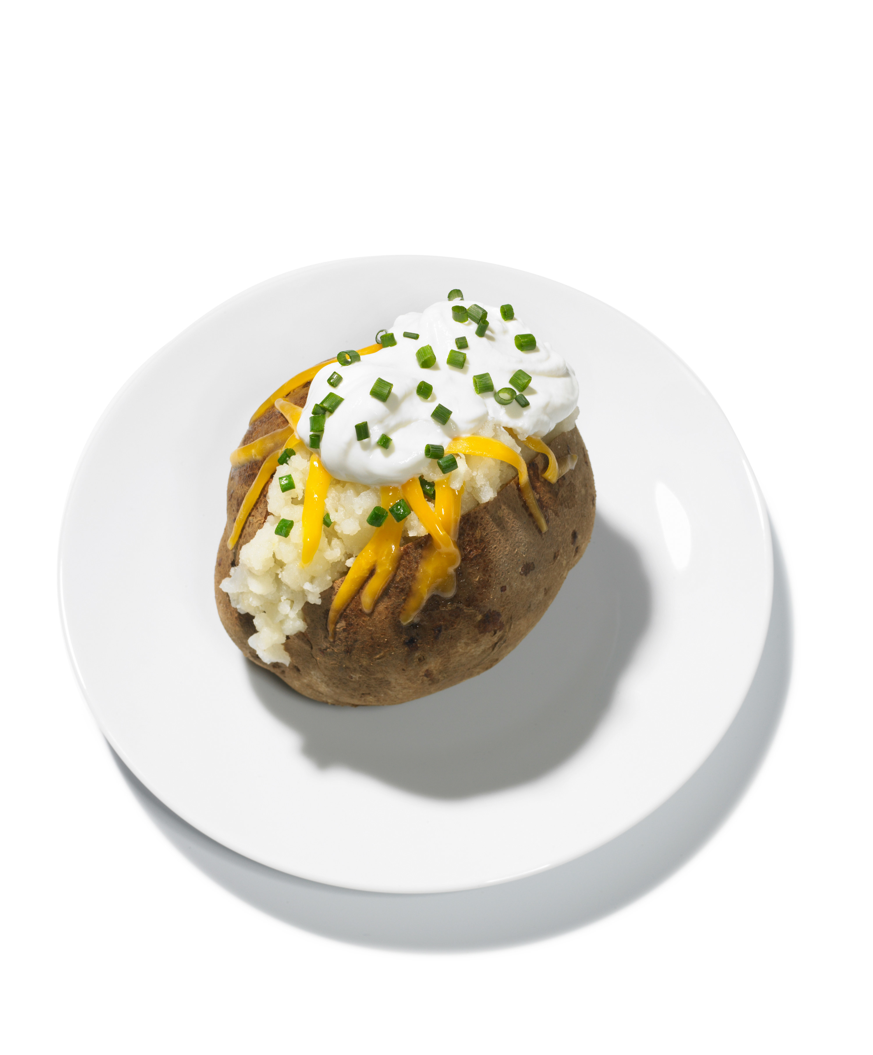 Baked potato with cheese, chives, and sour cream on a white plate