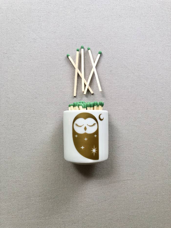 A small white jar of matches with a gold owl design