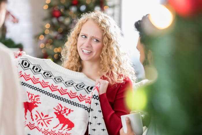 Woman makes a face while holding an ugly Christmas sweater