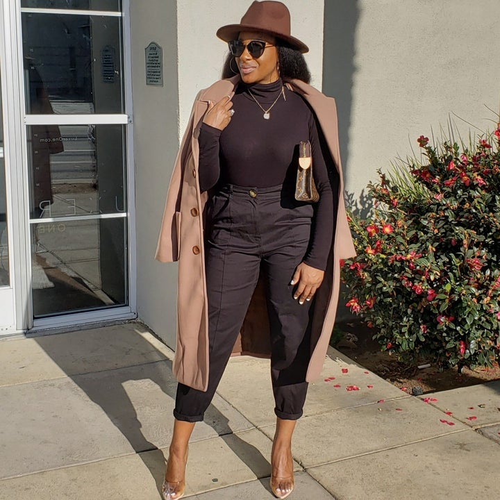 reviewer wearing the long coat in tan with an all black outfit and heels