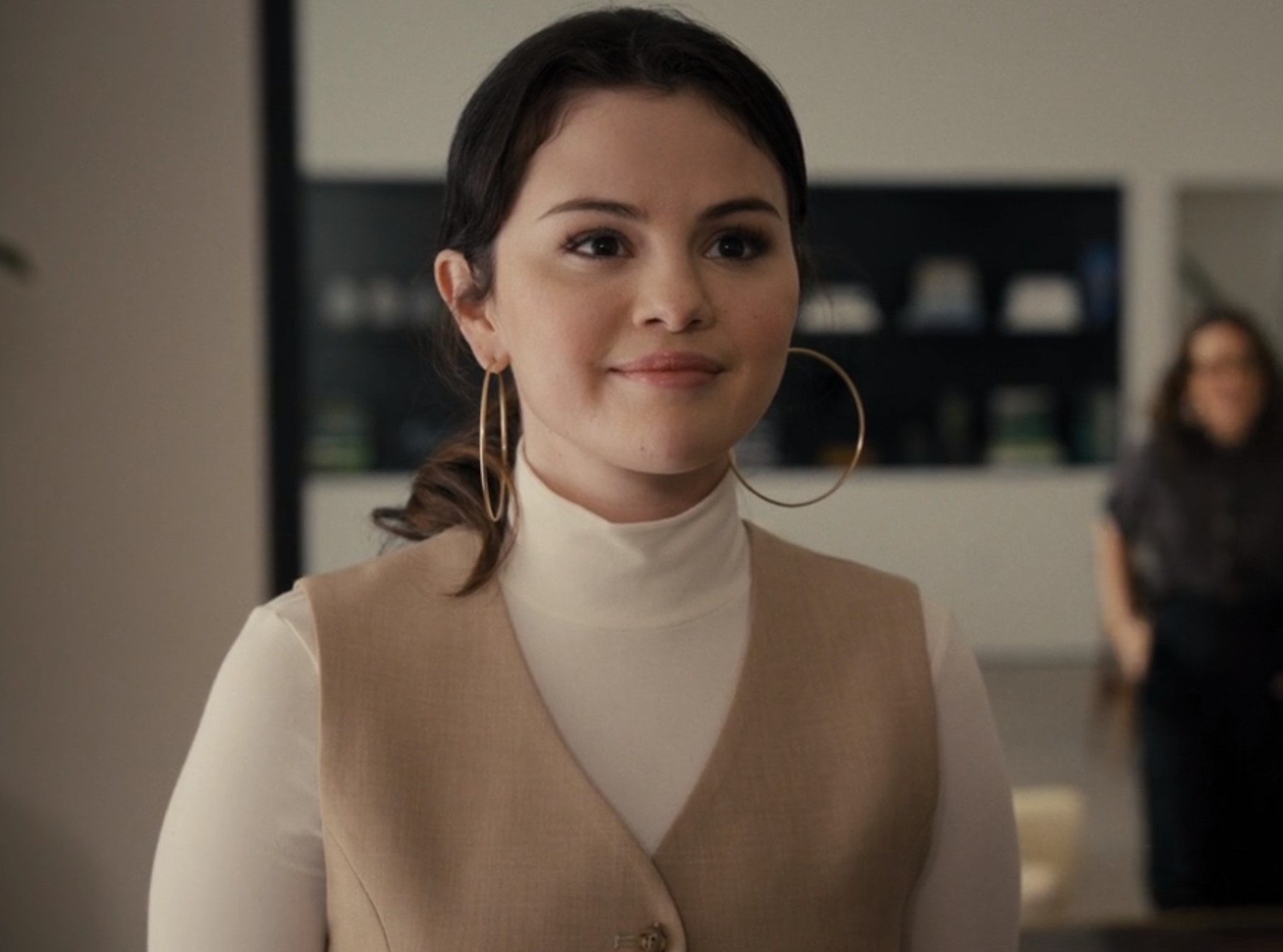 Photo of Selena Gomez as Mabel in a white turtleneck, a tan vest and pink lipstick