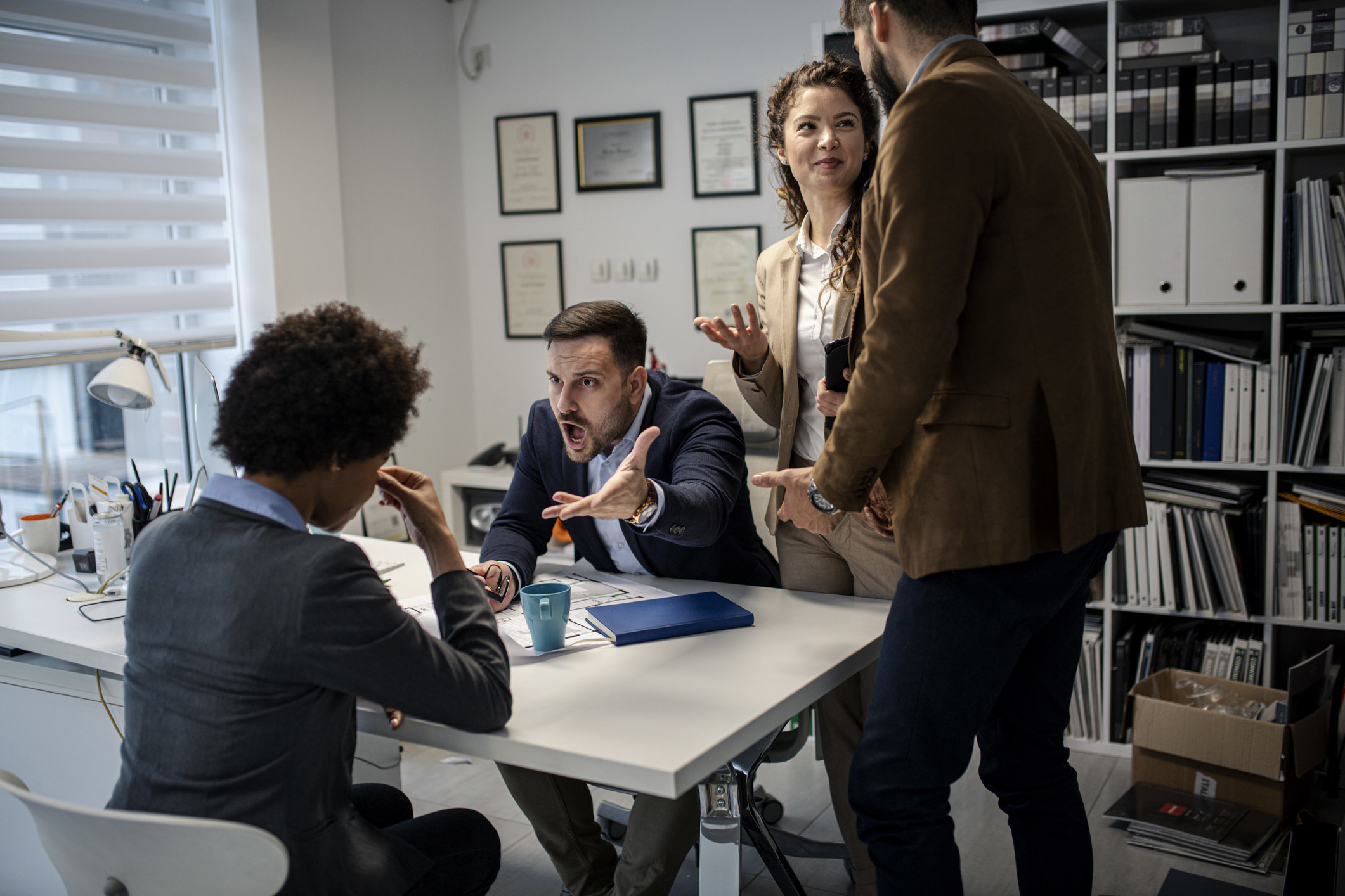 A woman being yelled at by her boss while too people smile and watch