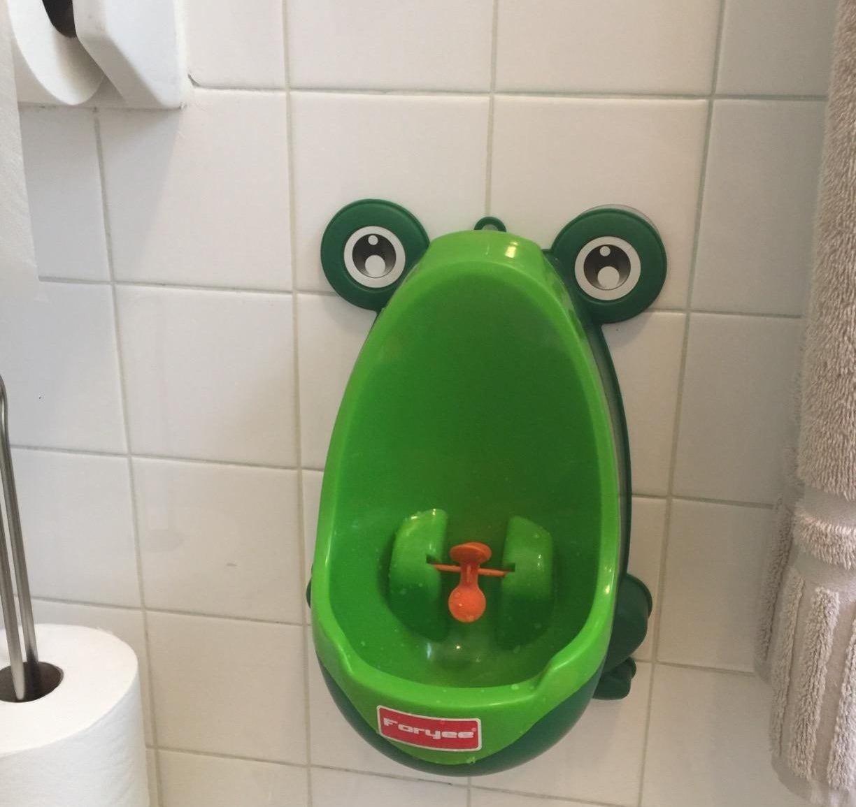 Reviewer&#x27;s photo showing the green urinal hanging on a tile wall