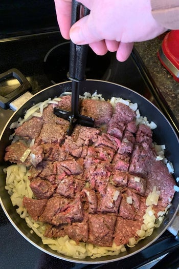 reviewer chopping ground beef in a pan with the long-handled, four-blade tool