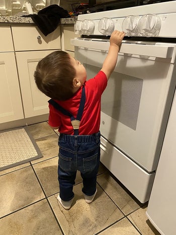 Reviewer's photo of their child reaching for the stove knobs fitted with clear covers