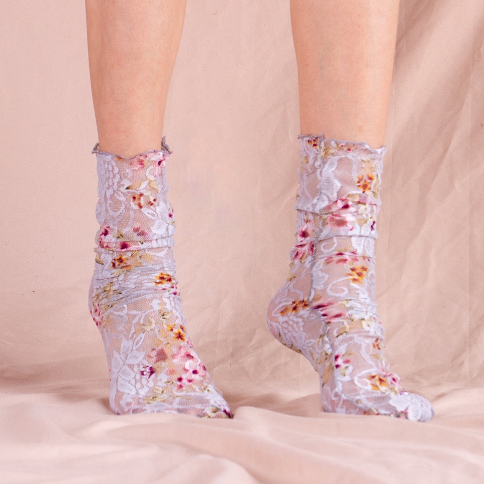 Two feet modeling gray mesh and lace socks with a floral pattern