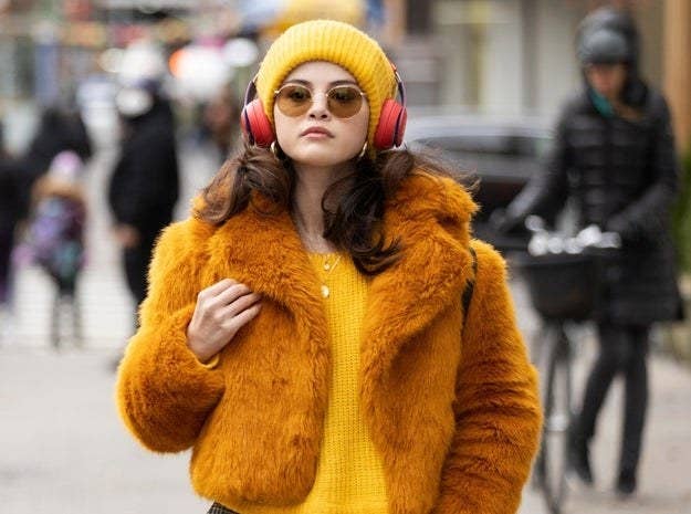Photo of Gomez as Mable in a yellow sweater, coat and headphones