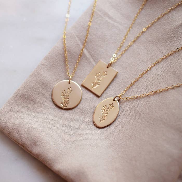 Three gold pendant necklaces with a floral patter on the pendant.