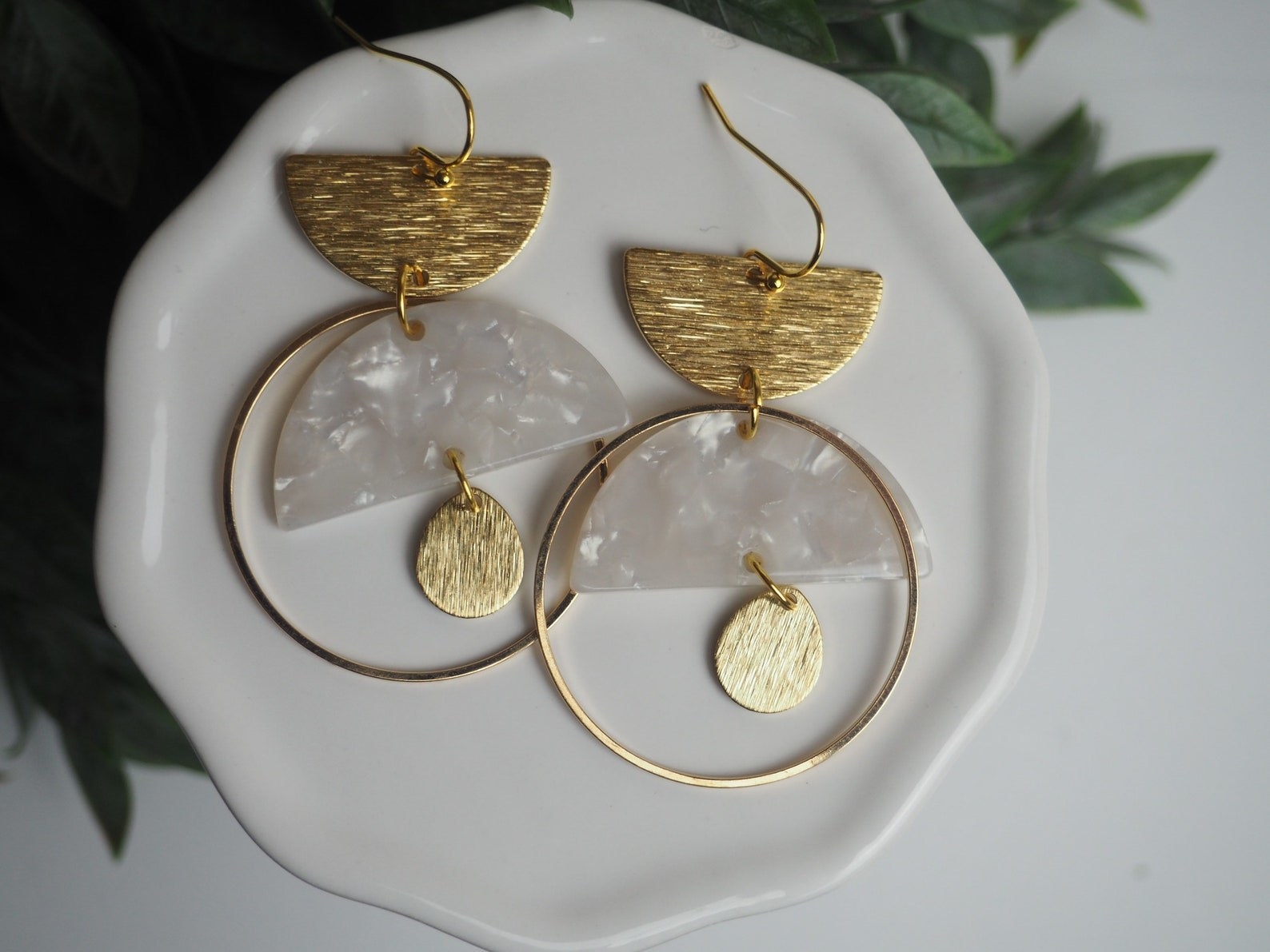 Gold dangling earrings with a white acrylic half-circle