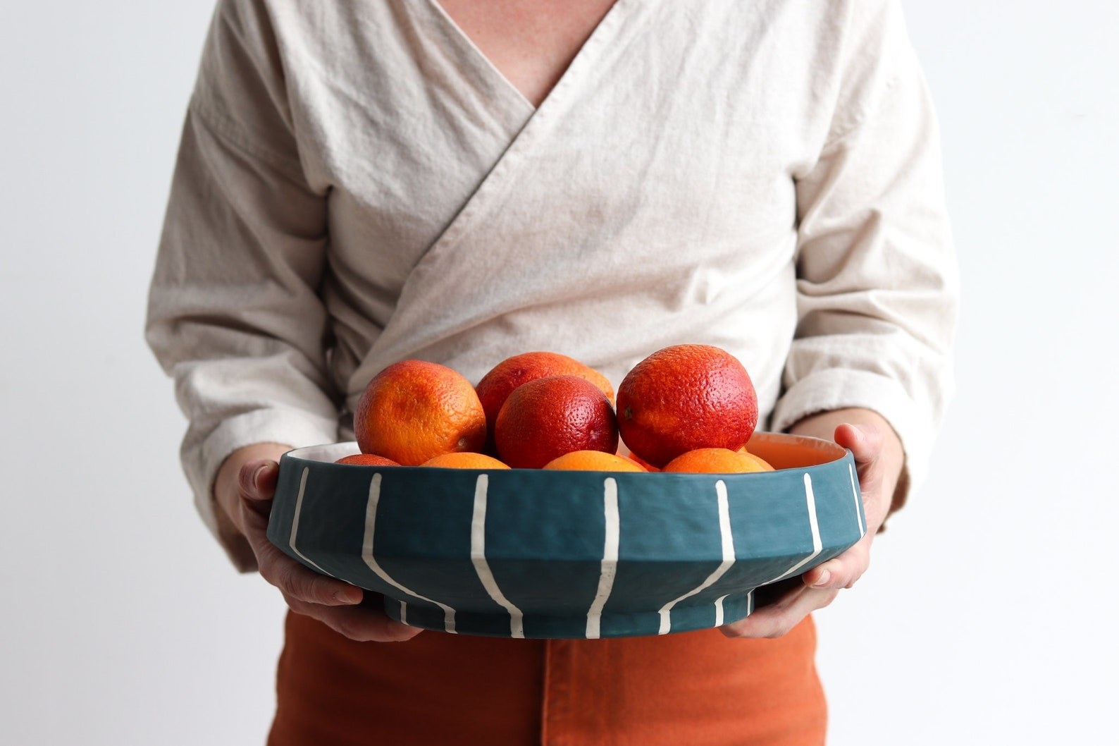 A woman holding a striped green and white serving bowl full of oranges