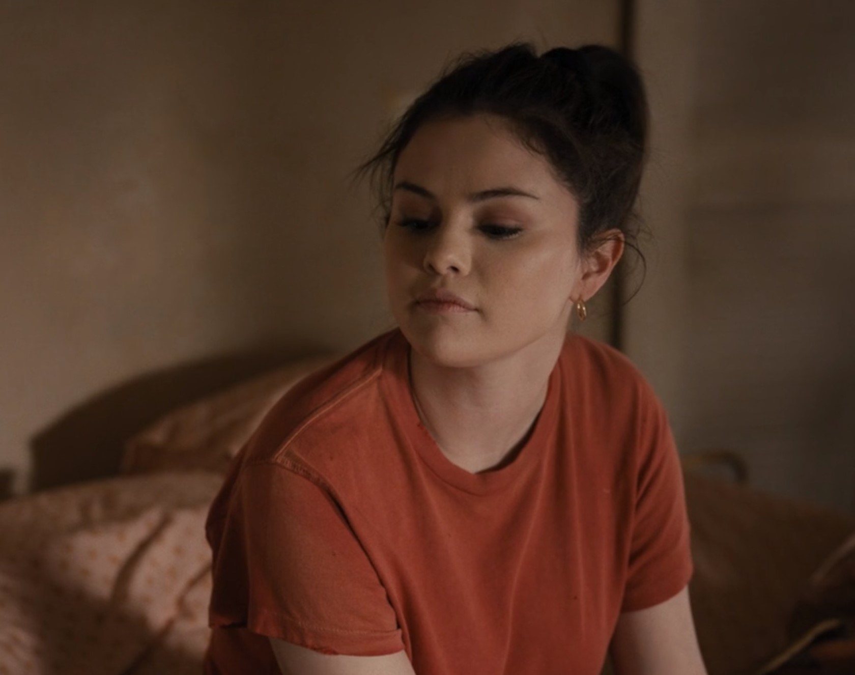 Photo of Selena Gomez as Mabel in a red shirt, gold accessories, and a dusty pink eyeshadow
