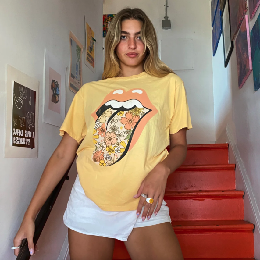 A model poses in the yellow Rolling Stones t-shirt with a floral tongue sticking out of orange lips.